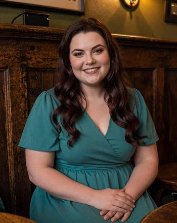 Caoimhe, 31, Irish woman from Dublin sitting in a cozy traditional Irish pub with warm amber lighting